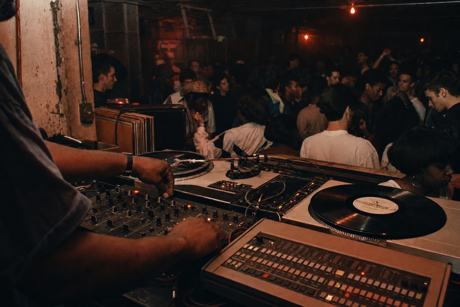 Detroit techno DJ booth details with drum machine sequencer vinyl records and dancers in a dark room